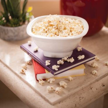 Nordic Ware white microwave popcorn popper bowl filled with fluffy popped kernels on stacked books