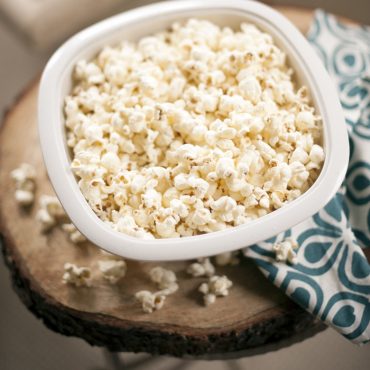 Nordic Ware white microwave popcorn popper filled with fluffy popped kernels, overhead view on wooden surface