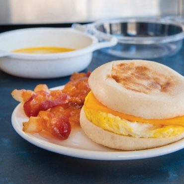 Breakfast sandwich with melted cheese and cooked egg on toasted English muffin with crispy bacon strips