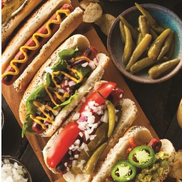 Nordic Ware aluminum hot dog steamer with cooked hot dogs and buns on serving platter with condiments