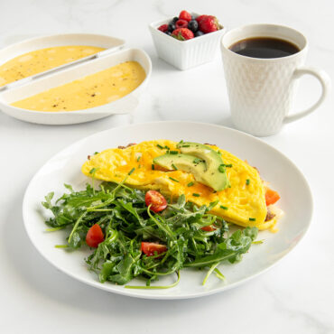 Nordic Ware omelet pan with fluffy cooked omelet, fresh berries, and coffee in styled kitchen setting
