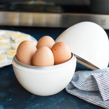 Nordic Ware white plastic egg boiler with lid open, containing six hard-boiled brown eggs