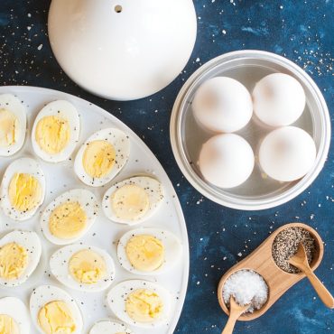 Nordic Ware white plastic egg boiler with cooked eggs inside, sliced hard-boiled eggs arranged on white plate