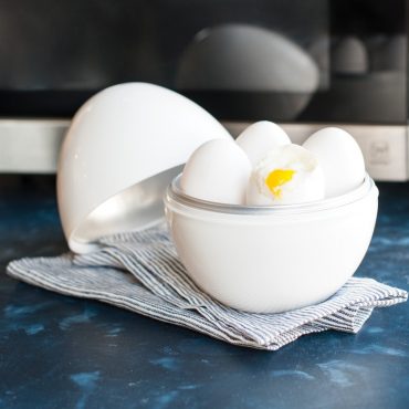 White ceramic egg boiler with soft-boiled eggs, one cracked open revealing runny yellow yolk