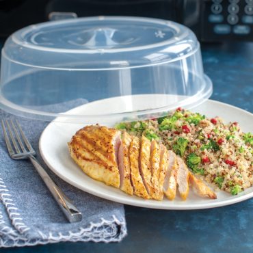 White microwave-safe plate with grilled chicken and quinoa salad, topped with clear vented splatter cover