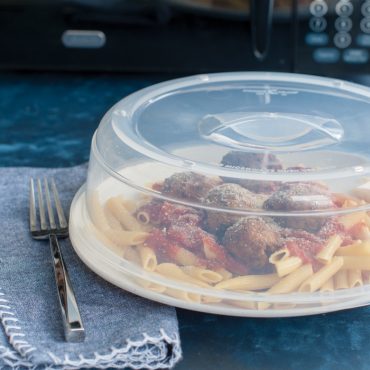 Nordic Ware clear plastic spatter cover over plate of pasta with meatballs and marinara sauce