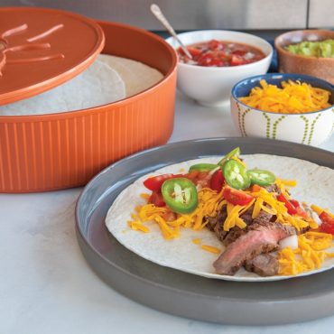 Nordic Ware orange tortilla warmer with lid open showing stack of tortillas, taco plate with beef and toppings