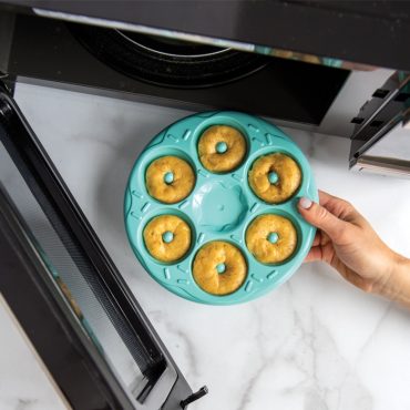 Hand placing Nordic Ware Donut Bites pan filled with raw batter into microwave, showing 12 mini donut cavities