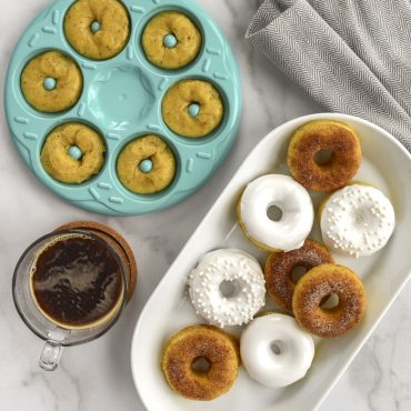 Nordic Ware aluminum donut bites pan with raw batter in cavities, beside plate of glazed mini donuts and coffee cup