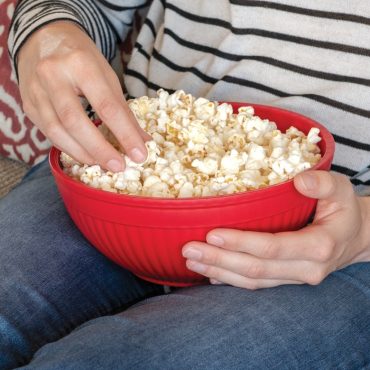 Person in striped shirt holding red Nordic Ware Quick Pop popcorn bowl filled with fresh white popcorn