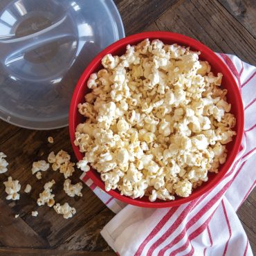 Red Nordic Ware Quick Pop microwave popcorn maker filled with fresh white popped kernels, clear lid nearby
