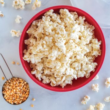 Red Nordic Ware Quick Pop bowl filled with fluffy white popcorn, small cup of kernels beside it