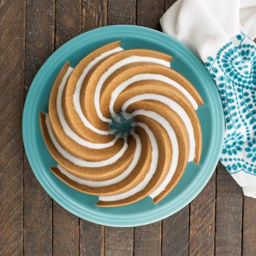 Golden bundt cake with white glaze drizzle baked in Nordic Ware Heritage bundt pan, showing spiral fluted design