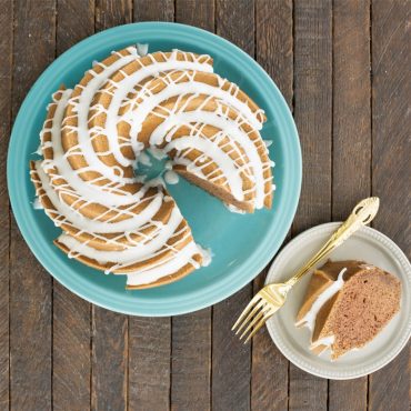Sliced bundt cake with white glaze drizzle on turquoise plate, showing Nordic Ware Heritage pan's detailed fluted pattern