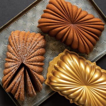 Two golden loaf cakes with Nordic Ware aluminum fluted loaf pan, one dusted with powdered sugar and sliced