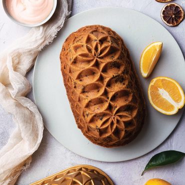 Golden baked loaf with intricate floral pattern from Nordic Ware Jubilee pan, served with orange slices