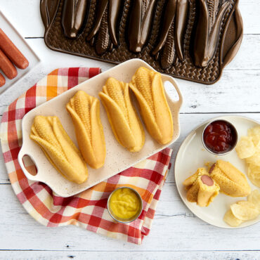 Golden cornbread corn dogs baked in Nordic Ware bronze aluminum corn cakes pan, shaped like corn cobs