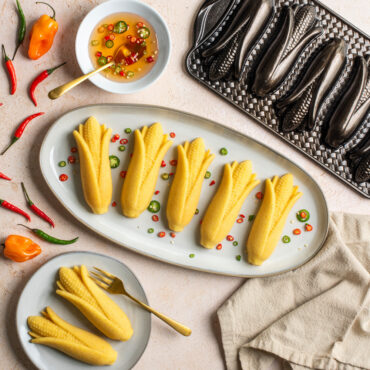 Plated Cornbread cakes with diced peppers surrounded by full peppers and dish of honey