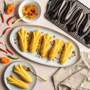Plated honey drizzled Cornbread cakes with diced peppers surrounded by full peppers and dish of honey