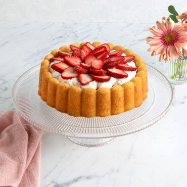 Charlotte cake with fluted sides baked in Nordic Ware pan, topped with whipped cream and fresh strawberry slices