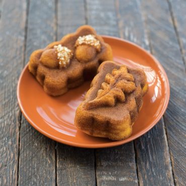 Two golden-brown mini spice loaves on white plate, baked in Nordic Ware Harvest mini loaf pan with chopped nuts