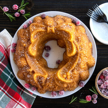 Golden bundt cake baked in Nordic Ware Holiday Wreath pan, dusted with powdered sugar and fresh cranberries