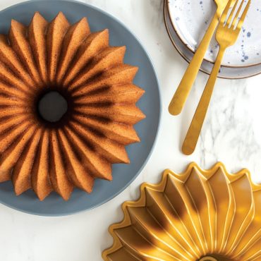 Golden spice bundt cake on white plate next to Nordic Ware Brilliance bundt pan with geometric fluted design