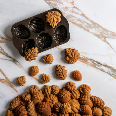 Small cakes baked in Nordic Ware Autumn Treats pan staged in a pile on a marble background