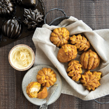 Small cakes baked in Nordic Ware Autumn Treats pan, one cake cut in half with butter spread on it