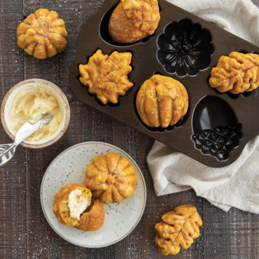 Small cakes baked in Nordic Ware Autumn Treats pan, one cake cut in half with butter spread on it