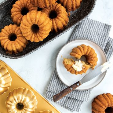 Golden-brown bundtlette cakes in Nordic Ware aluminum pan with fluted design, one served on white plate