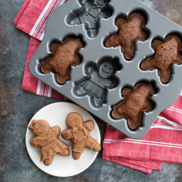 Nordic Ware aluminum gingerbread kids cakelet pan with 6 child-shaped cavities, natural finish, with baked golden brown gingerbread cakes