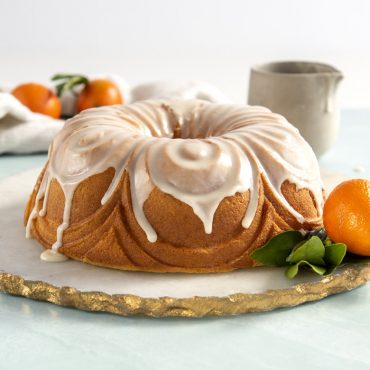 Golden bundt cake with white glaze dripping down fluted sides, garnished with fresh citrus and mint leaves