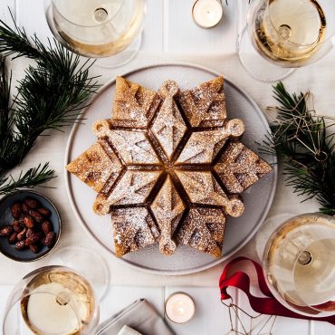 Baked snowflake-shaped cake with intricate ridged design, dusted with powdered sugar on white plate