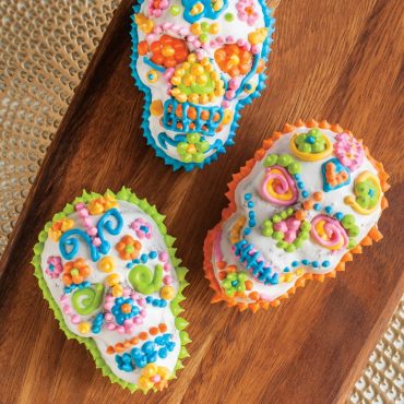 Six decorated skull cakelets with bright pink and orange piped frosting from Nordic Ware Haunted Skull pan