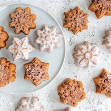 Six snowflake-shaped cakelets from Nordic Ware pan, some powdered sugar dusted, others glazed, on white plate
