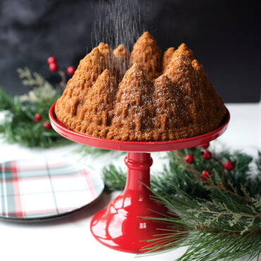 Golden bundt cake with pine tree design baked in Nordic Ware Pine Forest pan on red stand