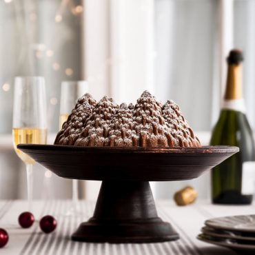 Golden spice bundt cake with pine tree design baked in Nordic Ware Pine Forest pan, dusted with powdered sugar on stand