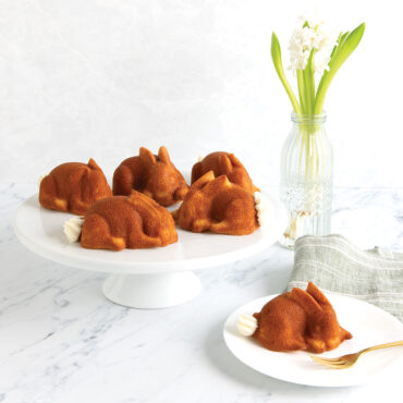 Two golden bunny-shaped cakes on white cake stand, baked in Nordic Ware aluminum bunny cake pan with detailed features