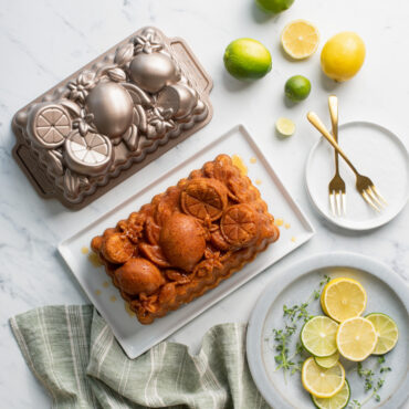 citrus blossom loaf cake on a white plate with whole and sliced lemons and limes