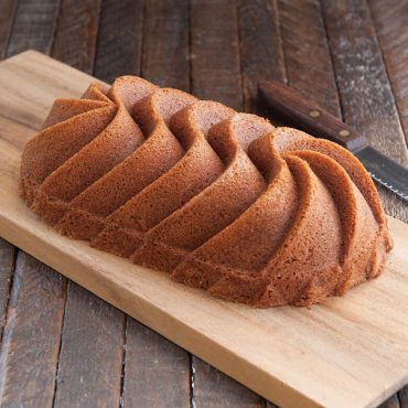 Golden vanilla loaf cake with decorative ridged pattern, sliced on wooden cutting board