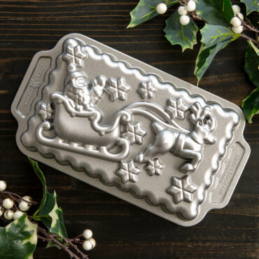 Nordic Ware aluminum Santa's sleigh loaf pan, detailed festive design, displayed with holiday candles and greenery