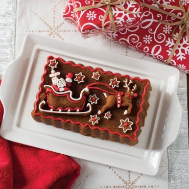Gingerbread loaf with festive red and white frosting piped in decorative patterns, sliced on white plate