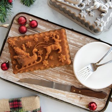 Golden loaf cake baked in Nordic Ware Santa's sleigh-shaped aluminum pan, displayed on wooden platter with festive setting