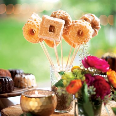 Golden geometric cakelets on sticks displayed in glass jar, showing detailed square and round shapes with hollow centers