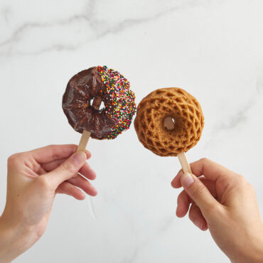 Two hands holding mini bundt cakes on sticks from Nordic Ware Geo Bundtlette pan, one chocolate glazed with sprinkles