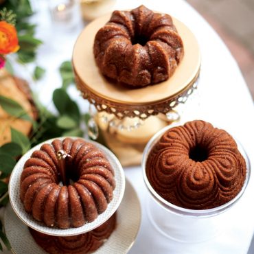 Three golden brown mini bundt cakes with detailed fluted ridges displayed on elegant cake stands