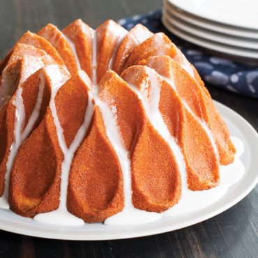 Golden bundt cake with white glaze drizzle, baked in Nordic Ware Crown bundt pan showing distinctive swirled pattern