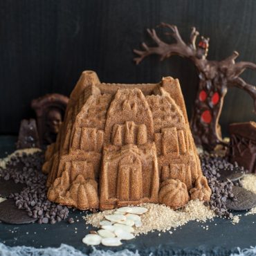 Spiced bundt cake from Nordic Ware Haunted Manor pan decorated as Halloween house with chocolate chip pathway and spooky tree backdrop