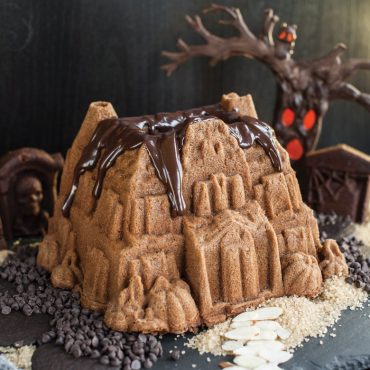 Haunted manor-shaped bundt cake with chocolate glaze, decorated with almonds and chocolate chips on counter